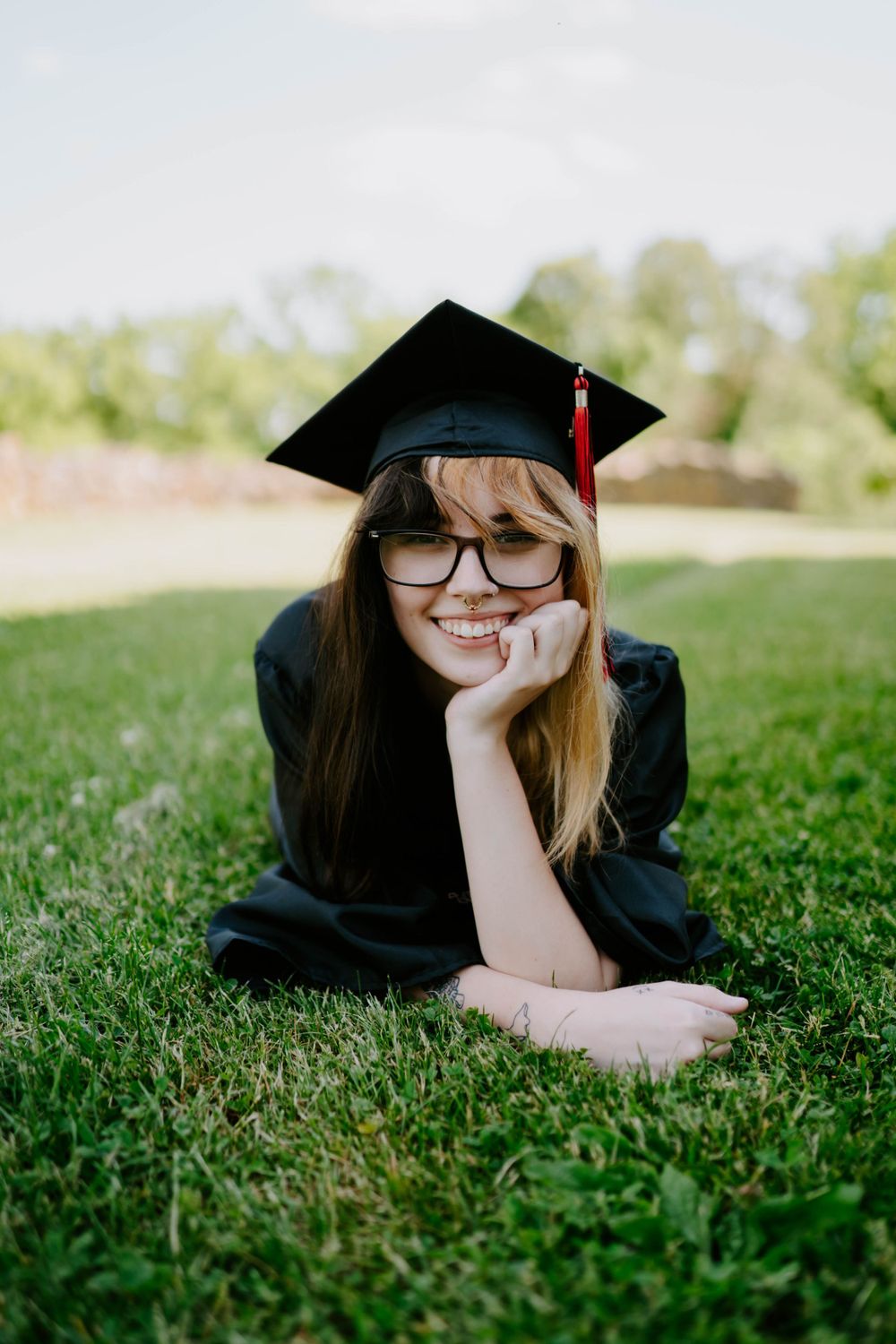 Graduate lying in green grass wearing traditional black cap and gown.