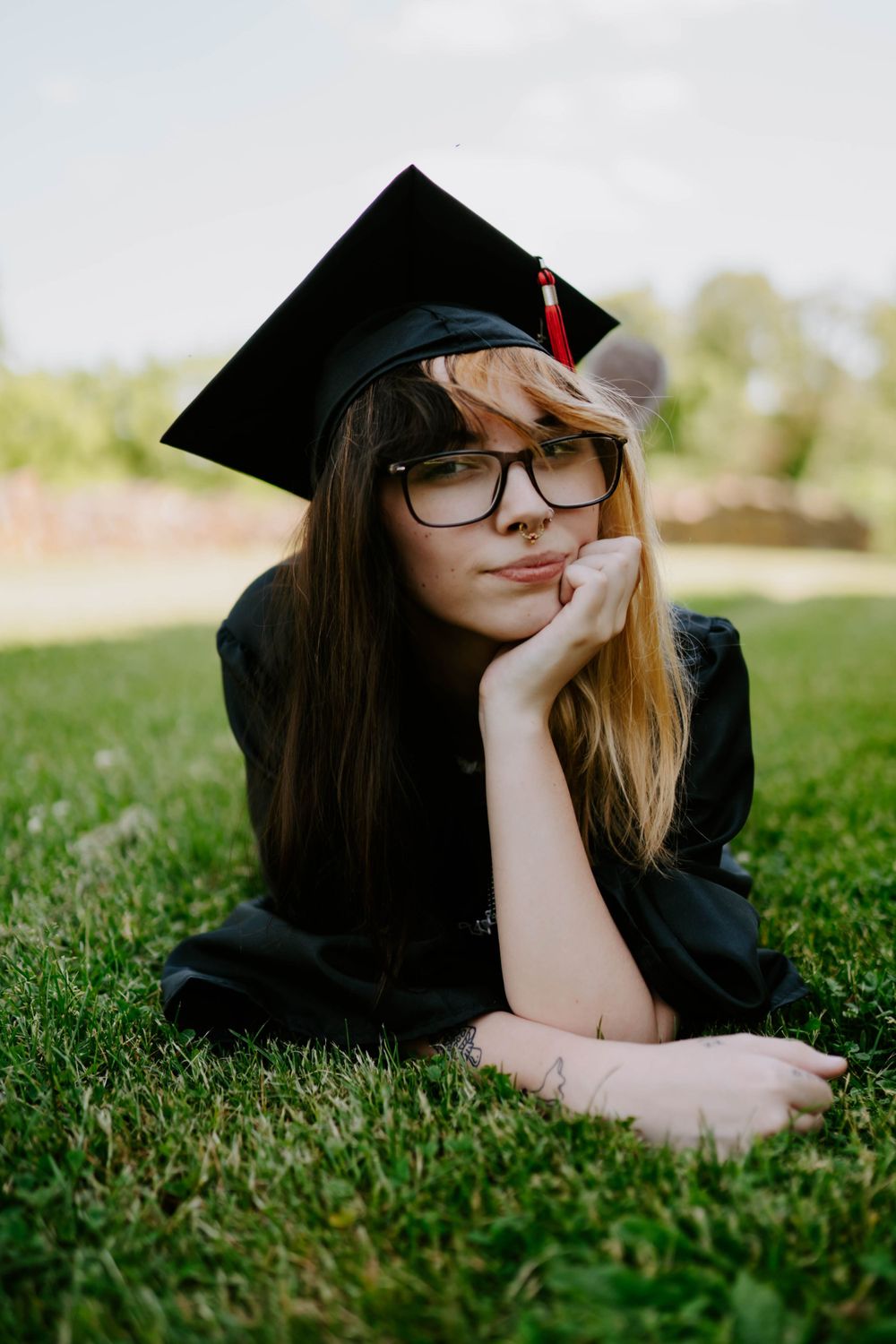 Student in graduation attire relaxing on green lawn during sunny day.