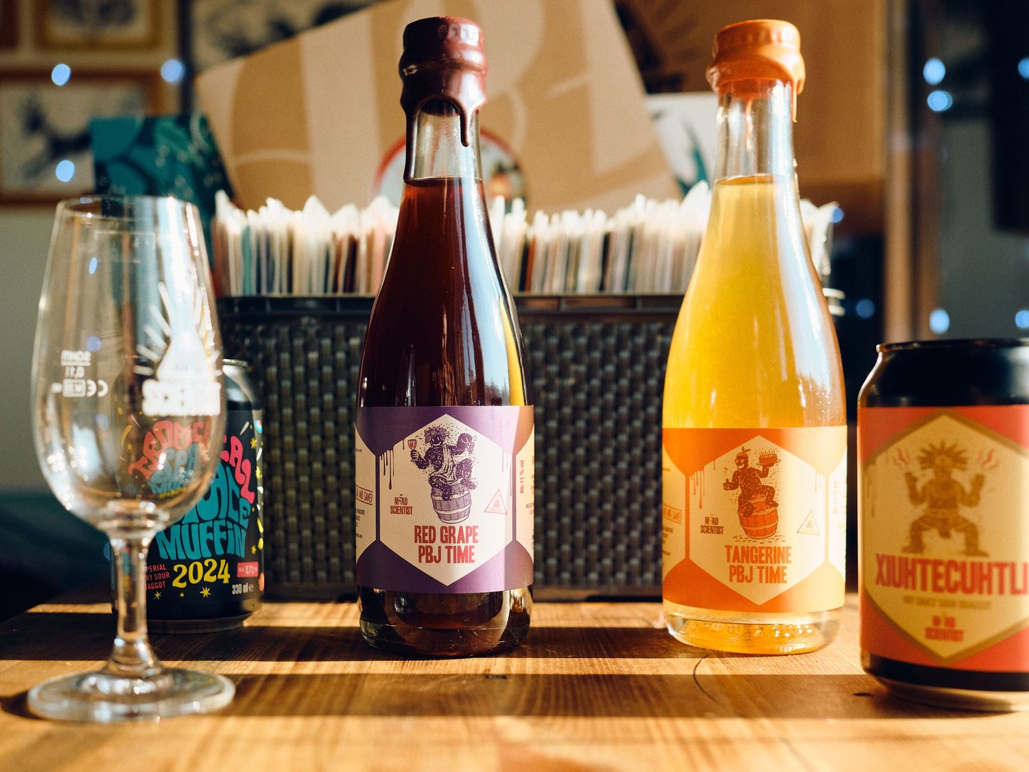Assorted colorful craft beer bottles and a wine glass arranged on a wooden table in a restaurant setting.
