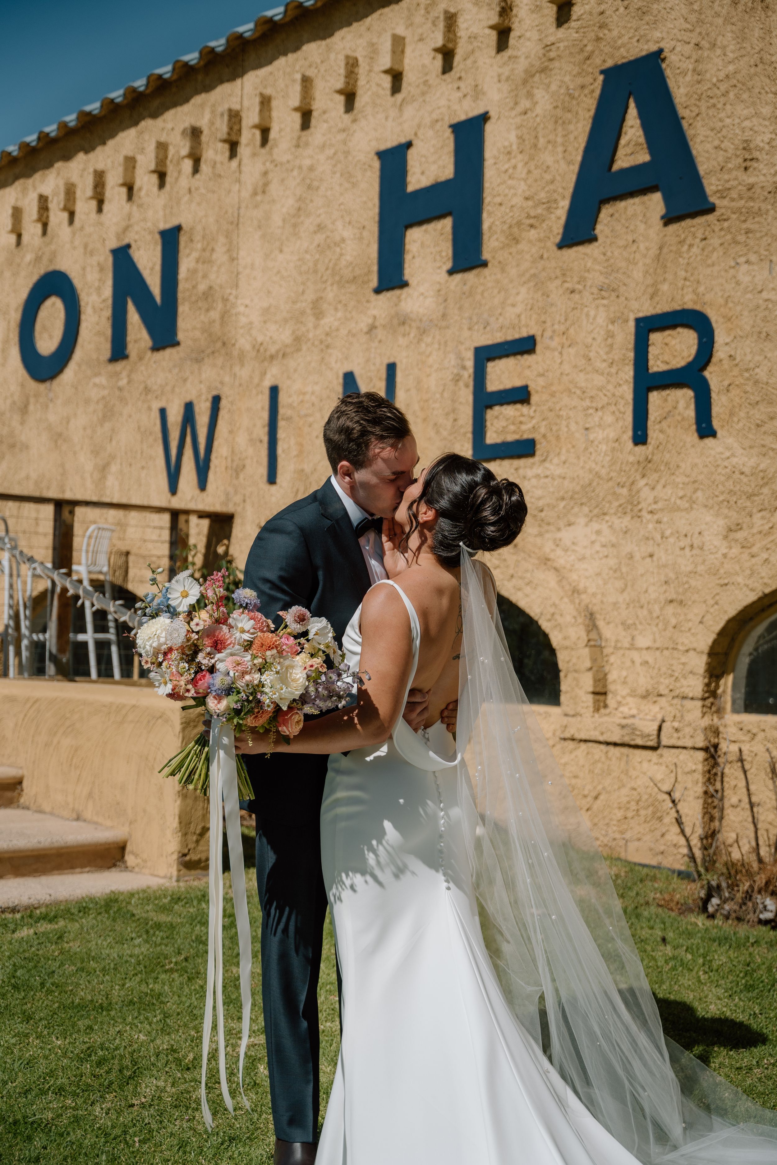 A romantic wedding moment unfolds against a rustic stone wall backdrop at a winery venue.