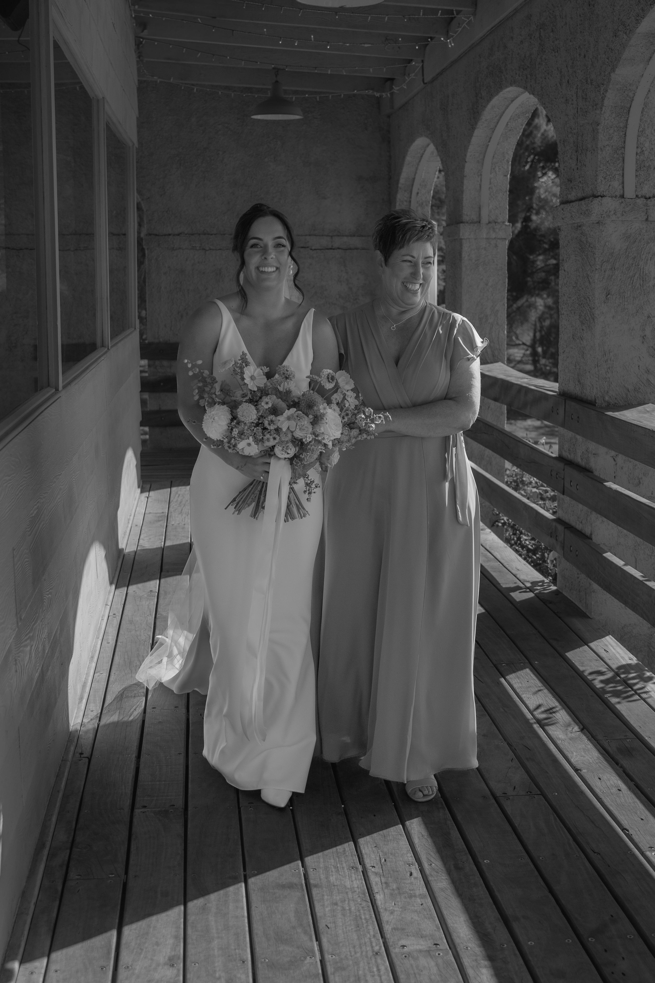Three people in light colored dresses stand together on a wooden deck in black and white.