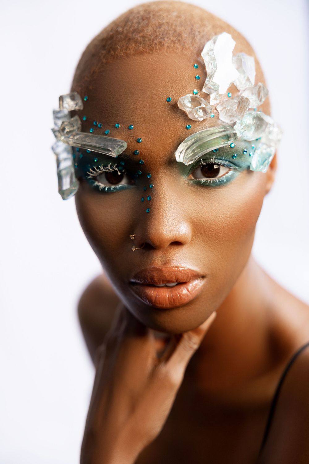 Close up beauty shot featuring pieces of recycled broken glass  placed above eyes along temples. Blue dramatic eye makeup compliments it.