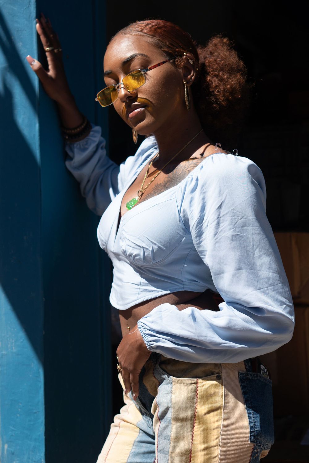 Casual street style portrait with white blouse and denim in natural sunlight. Woman looks down under 70s yellow sunglasses.