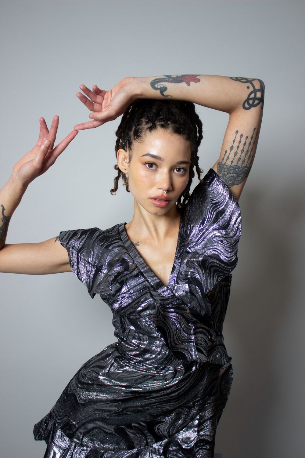 Artistic portrait of model in shimmering dress posed with one hand resting on their head and one finger touching another on the other hand.