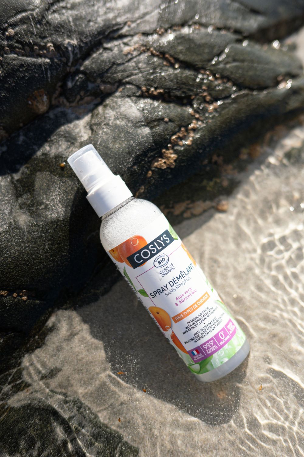 Produit en bouteille de pulvérisation naturelle Coslys placé sur des roches sombres et humides près de l'eau.