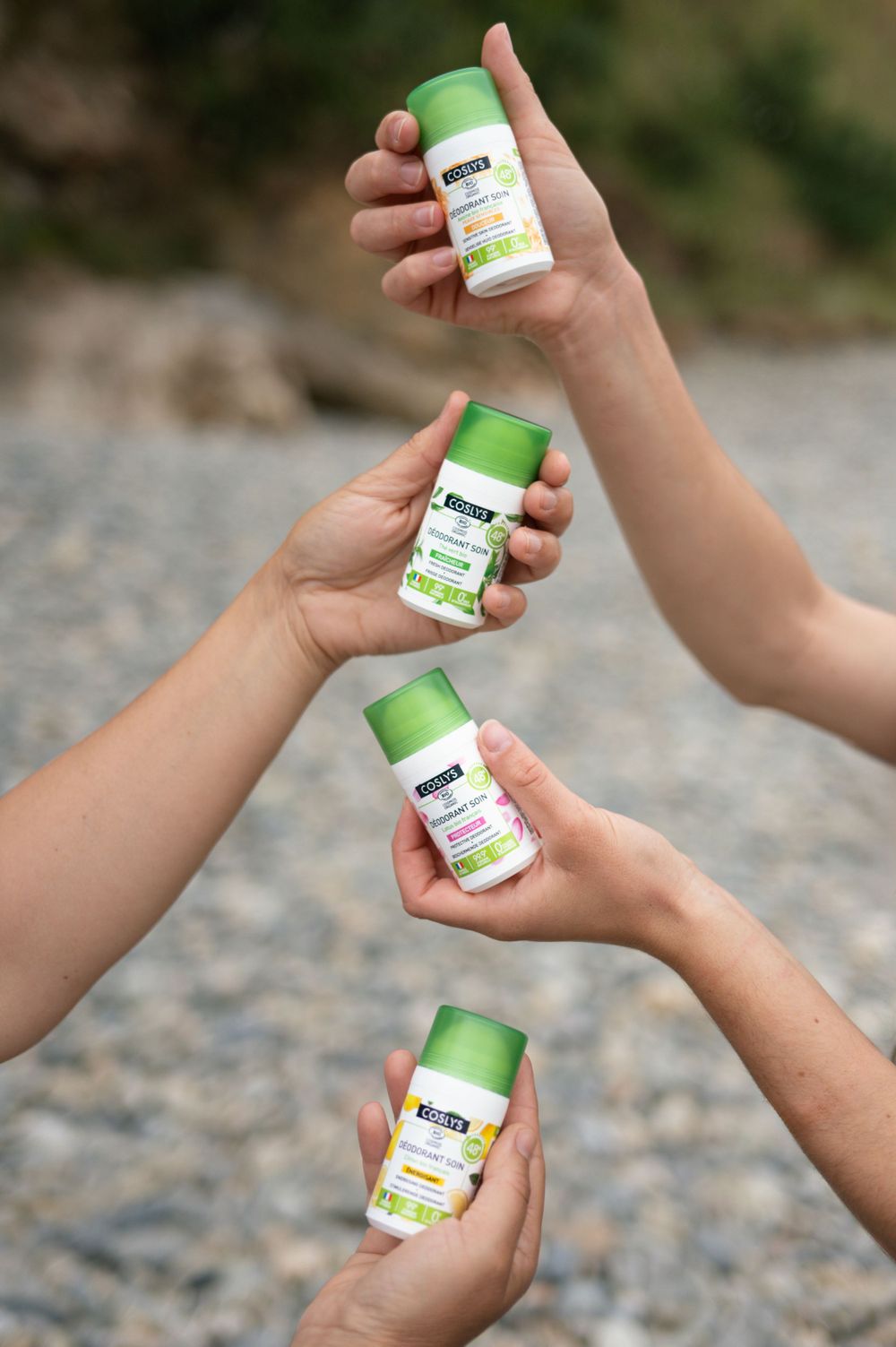 Plusieurs mains tenant des bouteilles de produits naturels verts sur fond rocheux.