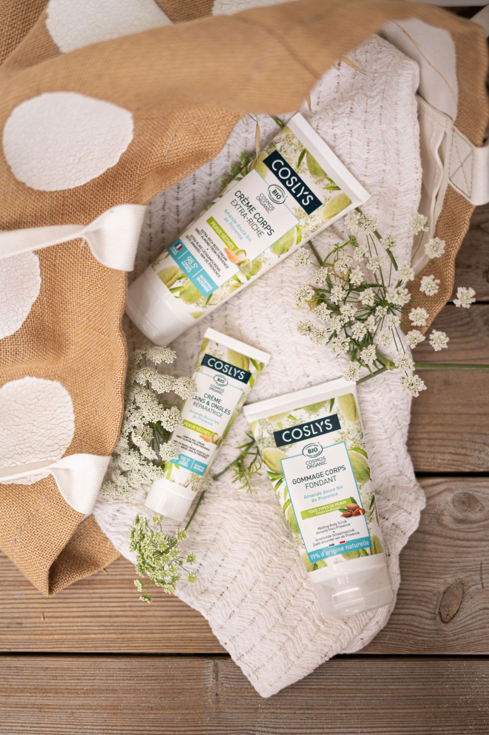 Produits de soins de la peau naturels disposés sur un tissu à pois avec des fleurs blanches et une surface en bois.