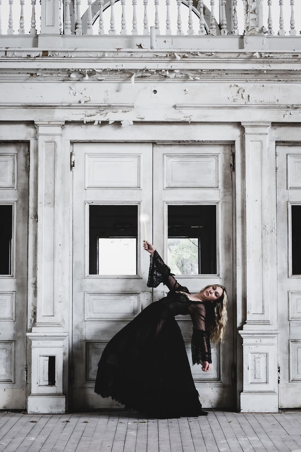 A witchy woman in a flowing black gown strikes a dramatic pose against ornate white doors in a vintage architectural setting.