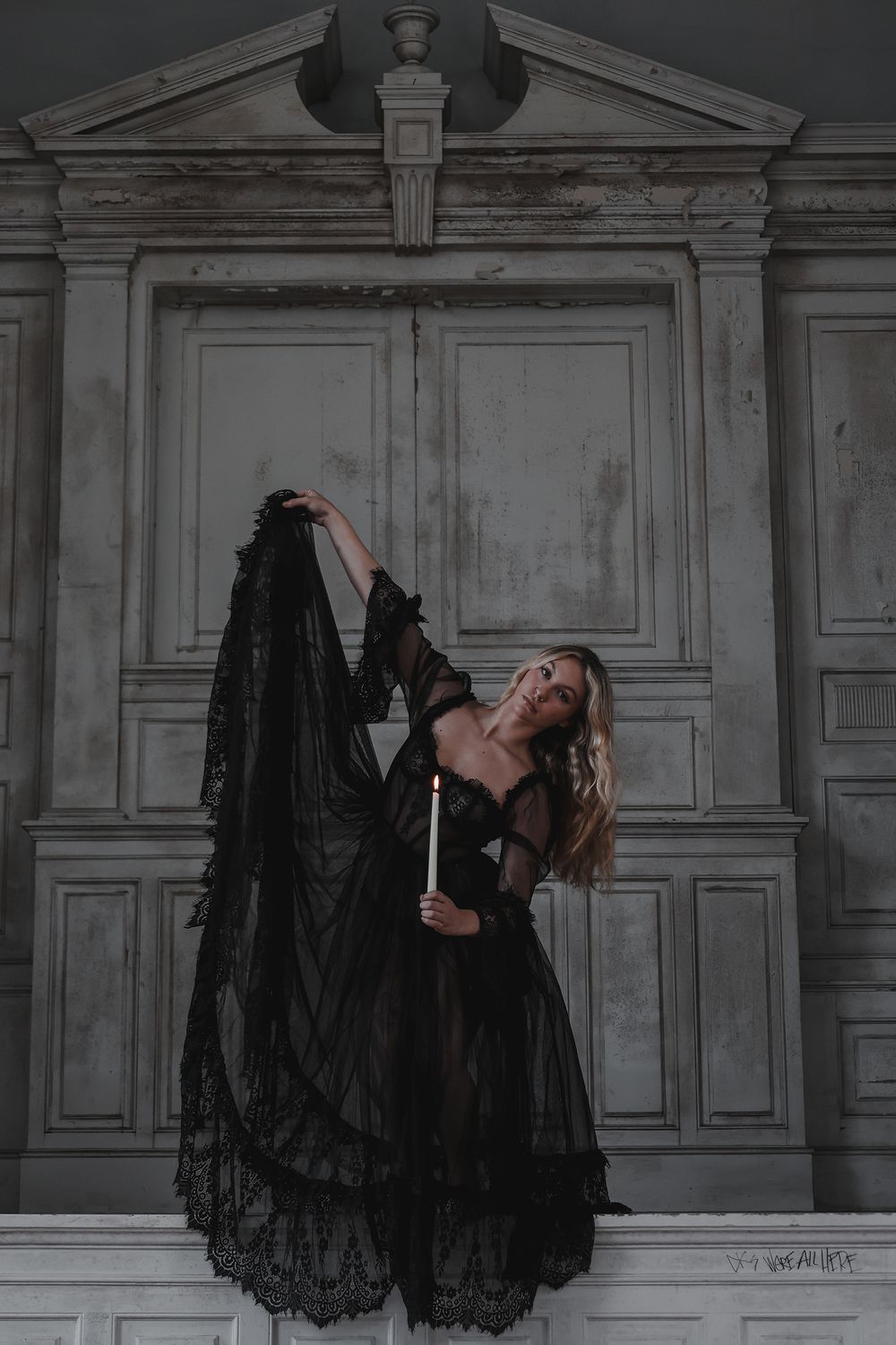 A witchy woman in a flowing black lace dress performs an elegant pose against a classical architectural backdrop.