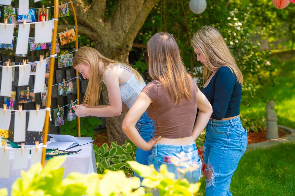 Students examine photos displayed on wood boards during an outdoor exhibition in a garden setting Quad Cities Graduation Event Photography