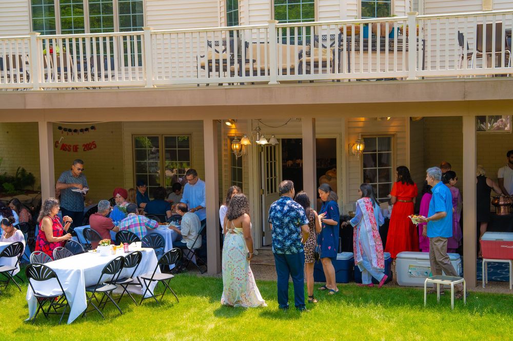 People gather on a lawn outside a white building with a porch for an outdoor social event. Quad Cities Graduation Event Photography