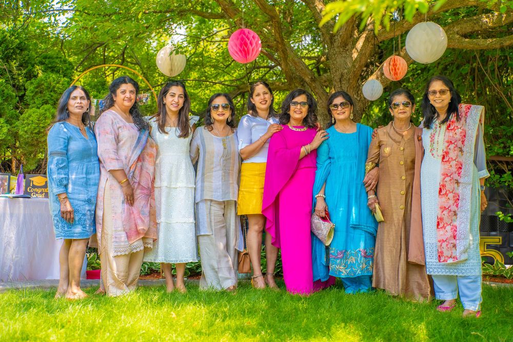 A group poses outdoors for photos in pastel and bright colored outfits with party lanterns and balloons in the background.