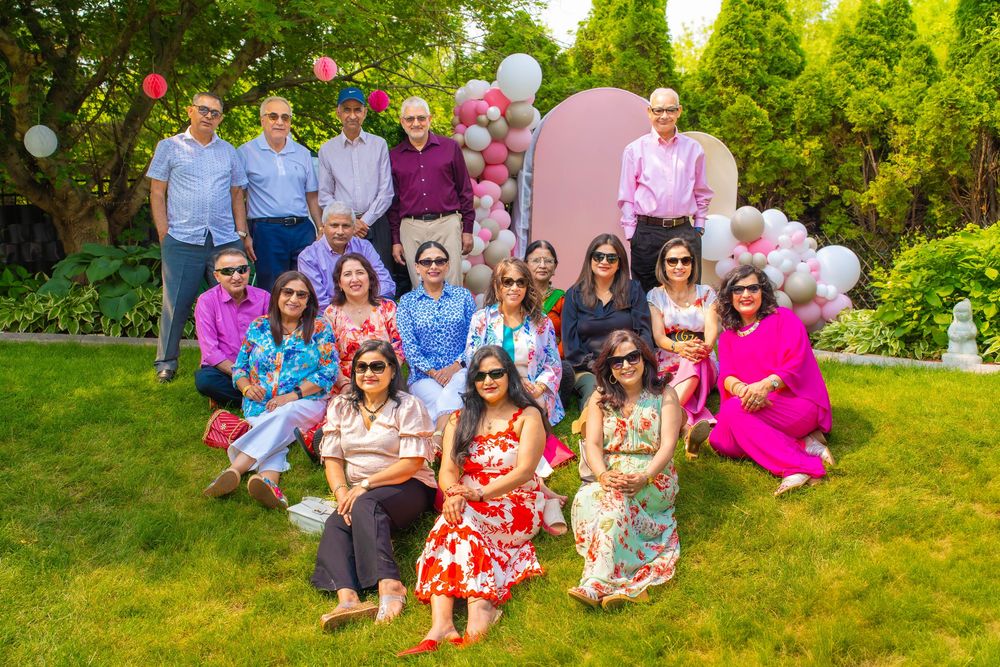 Large group gathering outdoors on a sunny day with green trees and pink decorations in background. Quad Cities Graduation Event Photography