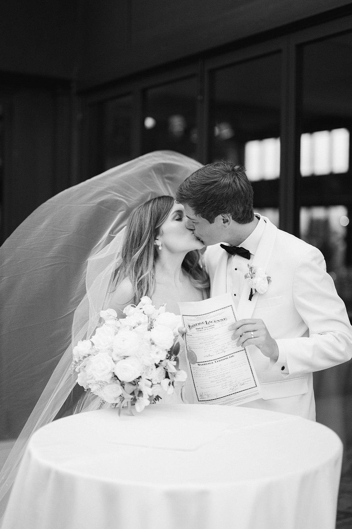 A romantic wedding moment with the couple sharing a kiss while holding a document.
