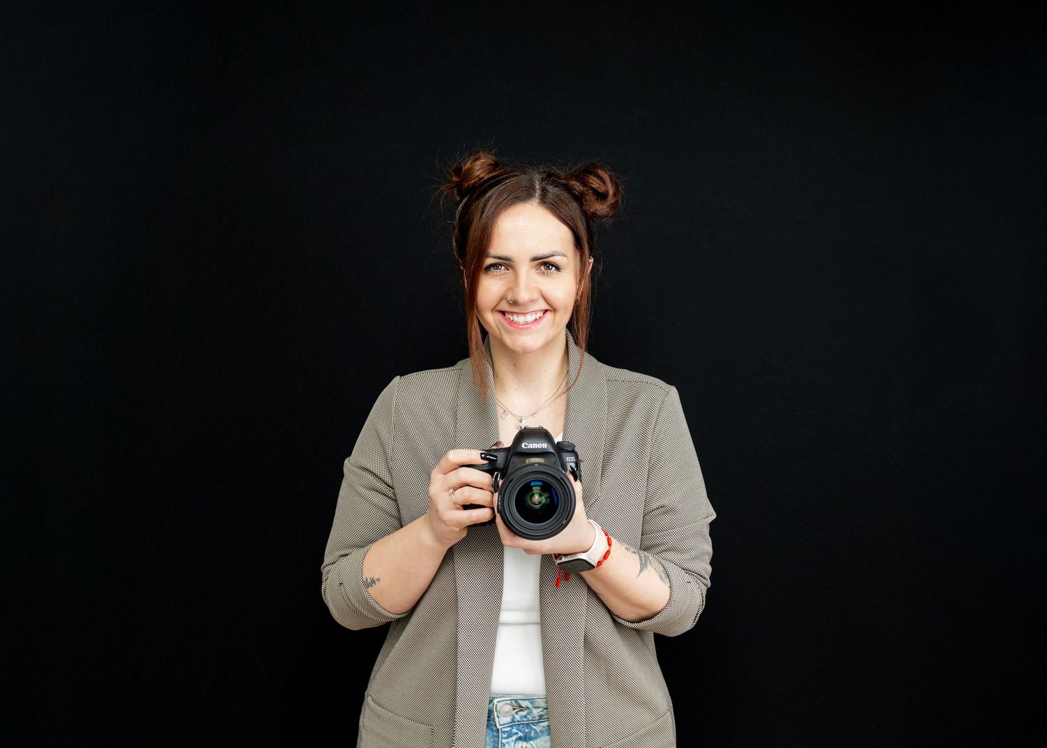 Professional photographer with camera wearing beige blazer against black background.