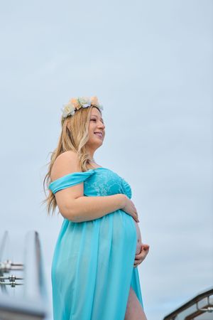 A person in a flowing turquoise dress poses outdoors against a cloudy sky in a series of connected photos.