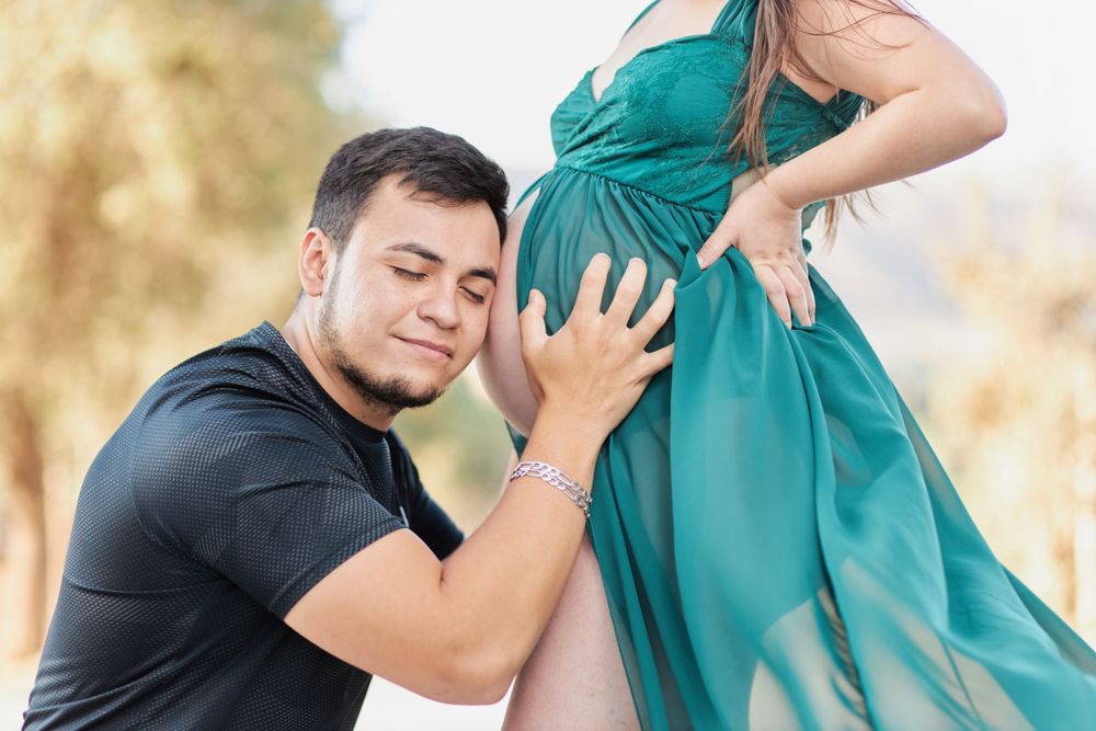 Intimate maternity photo with partner touching pregnant belly in outdoor setting.