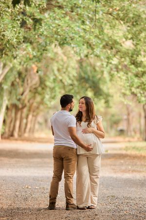 Family sits together on a path in a sun-dappled wooded area wearing coordinating neutral colored outfits.