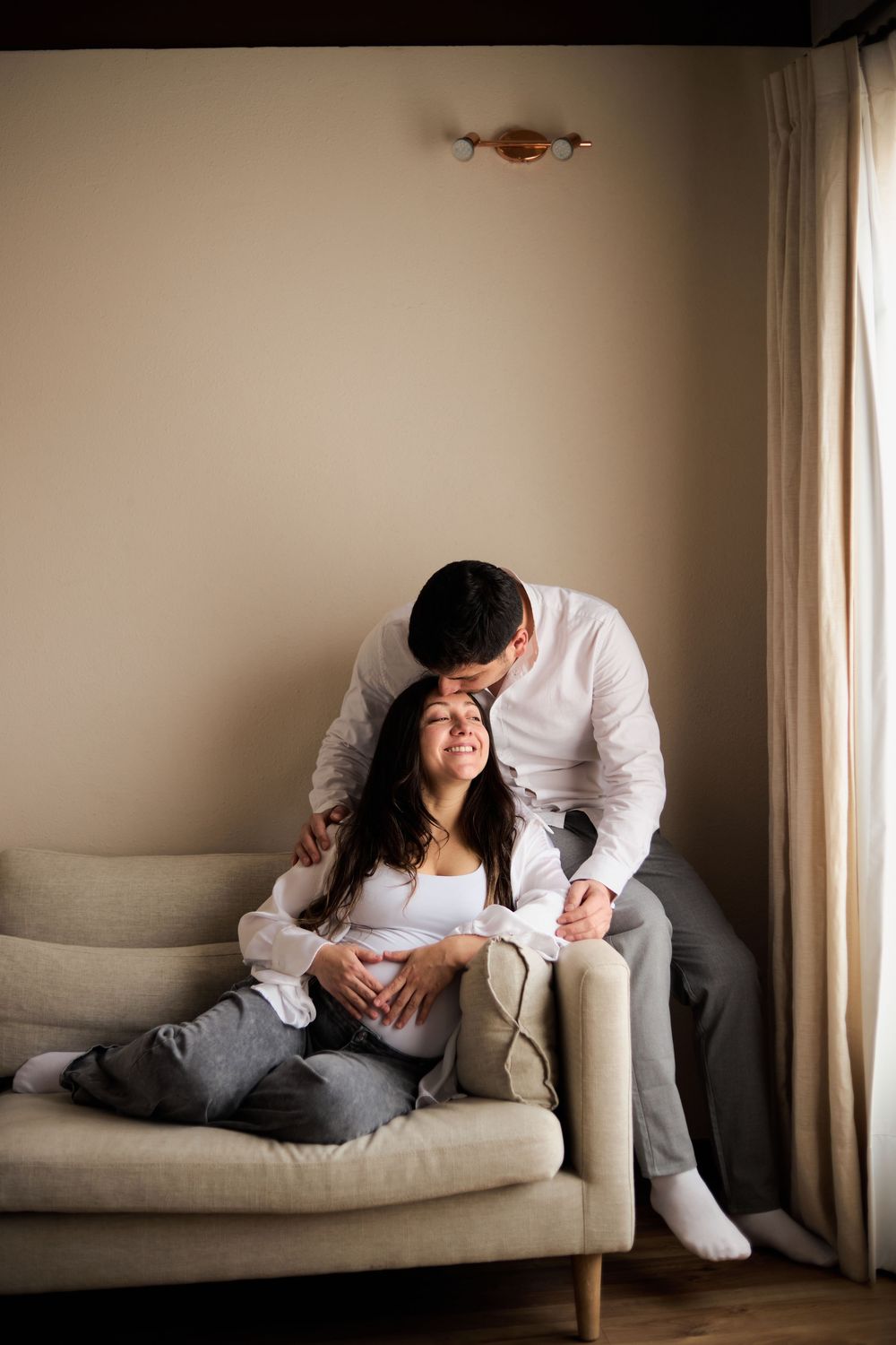 A series of four intimate photos showing two people in tender moments on a light gray couch near a window.