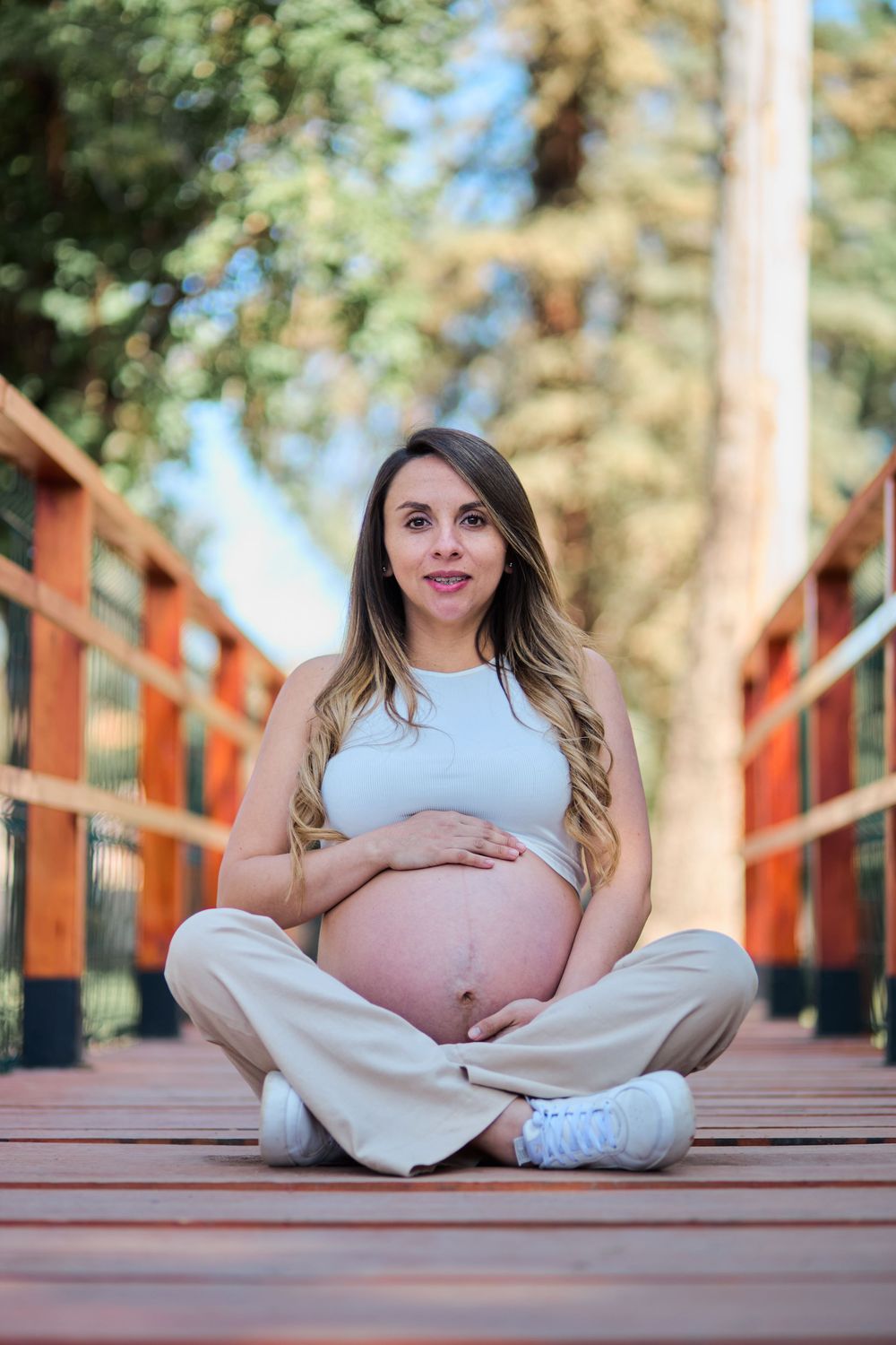 Maternity photo series showing a pregnant woman in white clothing sitting on wooden bridge deck in outdoor setting.
