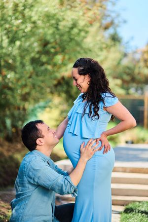 A couple in blue and denim outfits share a joyful moment outdoors during a pregnancy photoshoot.