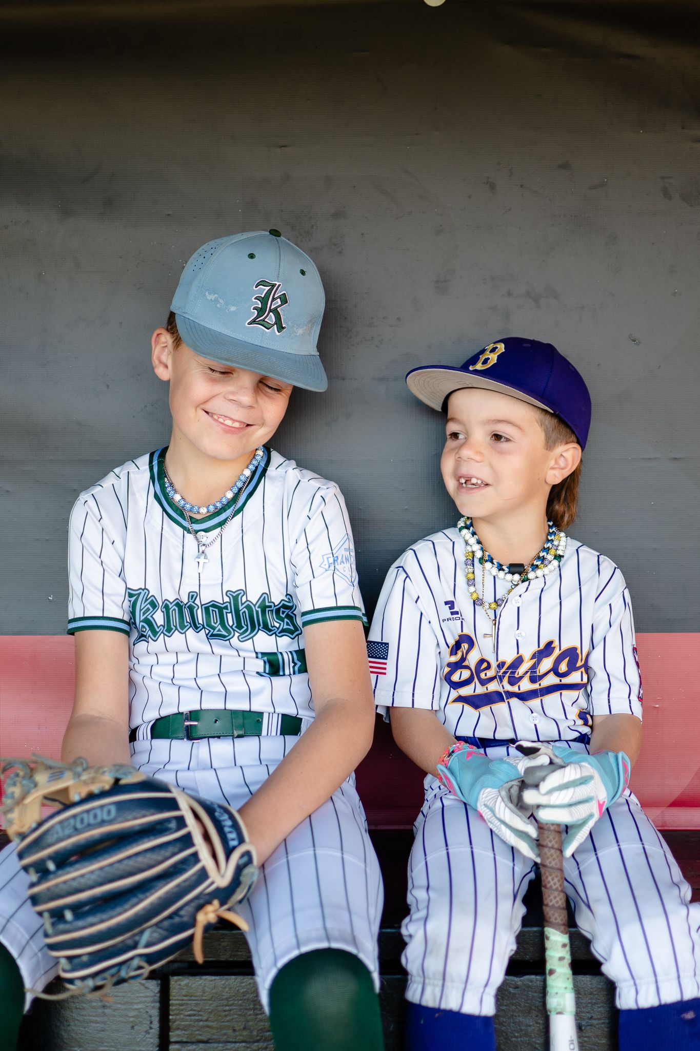 Two baseball players in pinstriped uniforms sit in a dugout with baseball gloves and gear.
