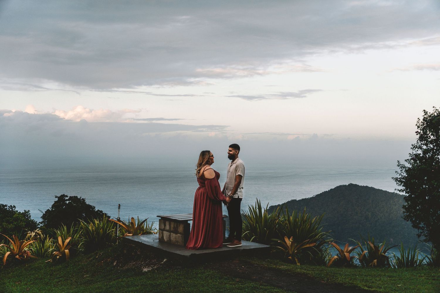 Couple standing on mountain overlook during cloudy sunset with ocean views.