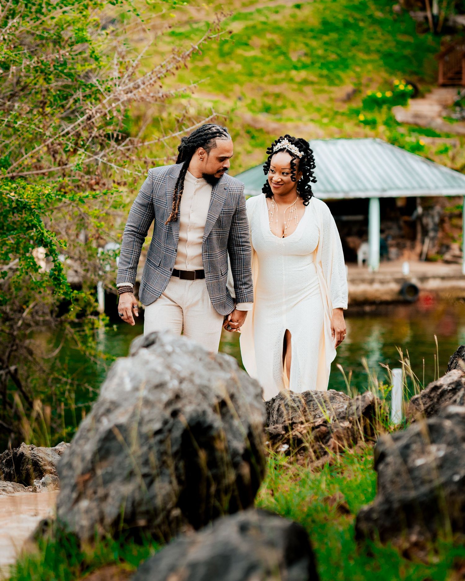 Romantic garden stroll with couple in formal attire near rustic lakeside cabin.