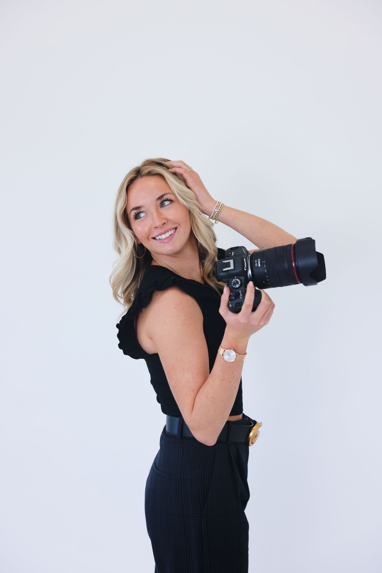 Portrait of photographer in black top and denim shorts holding camera outdoors.