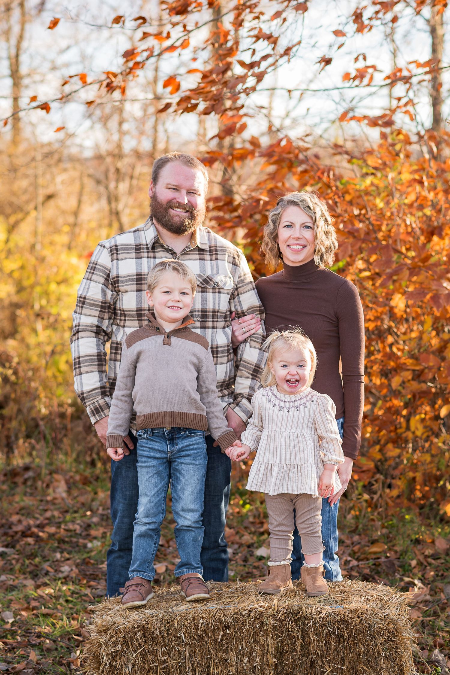 Family portrait on hay bale with autumn foliage in background.