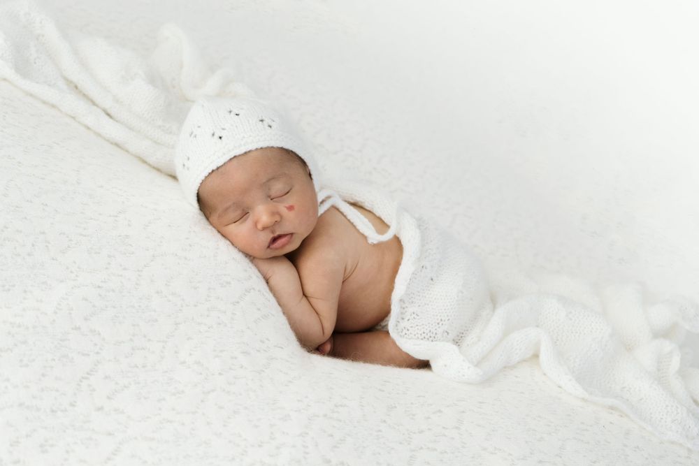 Un neonato addormentato avvolto in una coperta bianca giace pacificamente. Servizio newborn nel mio studio fotografico.