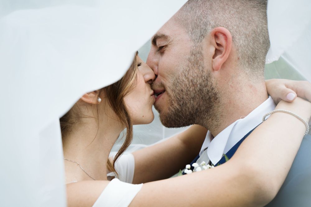 Primo piano di un romantico bacio di nozze sotto un velo bianco.