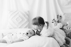 Bambina sorella che bacia dolcemente il fratello neonato sul letto con biancheria da letto bianca. Nel mio studio in provincia di AL.