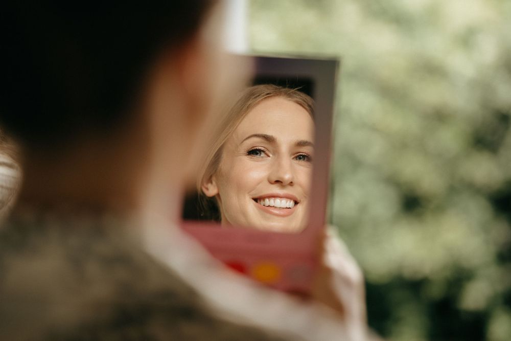 Close up reflection of a joyful smile in a handheld mirror during wedding preparations.