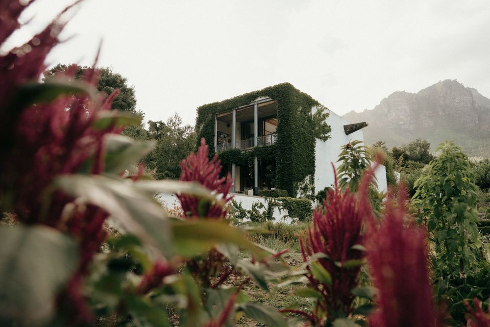 A rustic building with red flowers in the foreground and mountains visible in the distance.