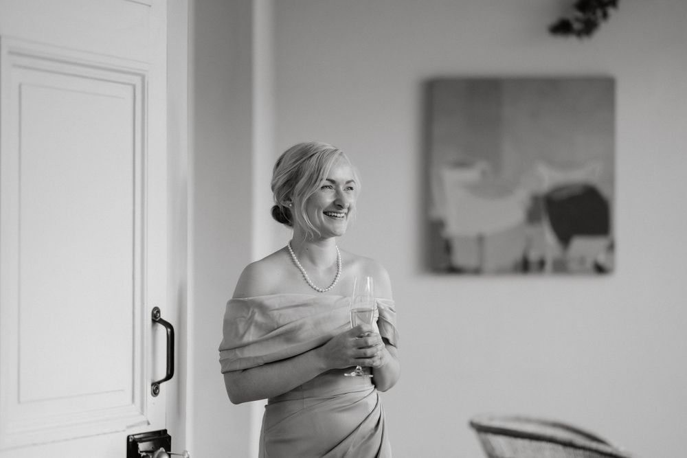 A candid black and white photograph showing a person laughing while getting ready indoors.