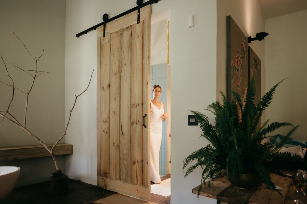 White wedding dress visible through sliding barn door with indoor plants.