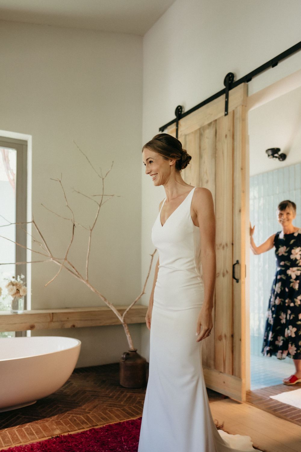 A bride in an elegant white gown stands in a modern bathroom with sliding barn door.