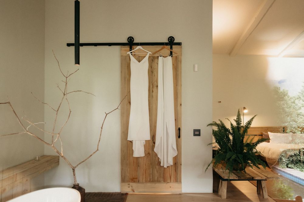 White dress hanging on rustic barn door with minimalist decor and plants.
