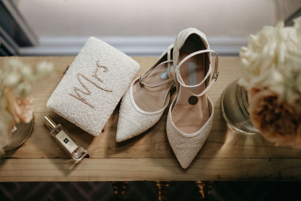 Wedding accessories including sparkly shoes and Mrs purse on wooden surface.
