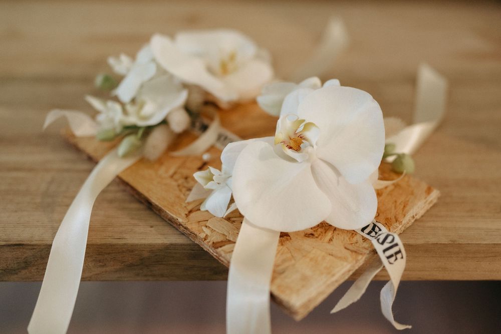 White orchid corsages with ribbons arranged on a wooden surface for a wedding.
