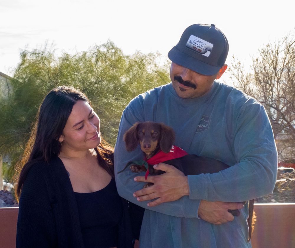 Couple admiring a dachshund puppy in a red bandana held by the man outdoors.