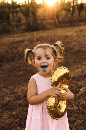 Dolce bimba al suo servizio fotografico smashcake 3 anni in Abito rosa su sfondo dorato al tramonto con palloncino numero tre.