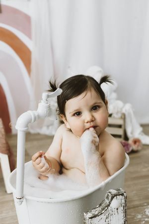 la bambina si gode il bagnetto in una vasca in stile vintage con bolle bianche ed elementi decorativi nel suo servizio smashcake.