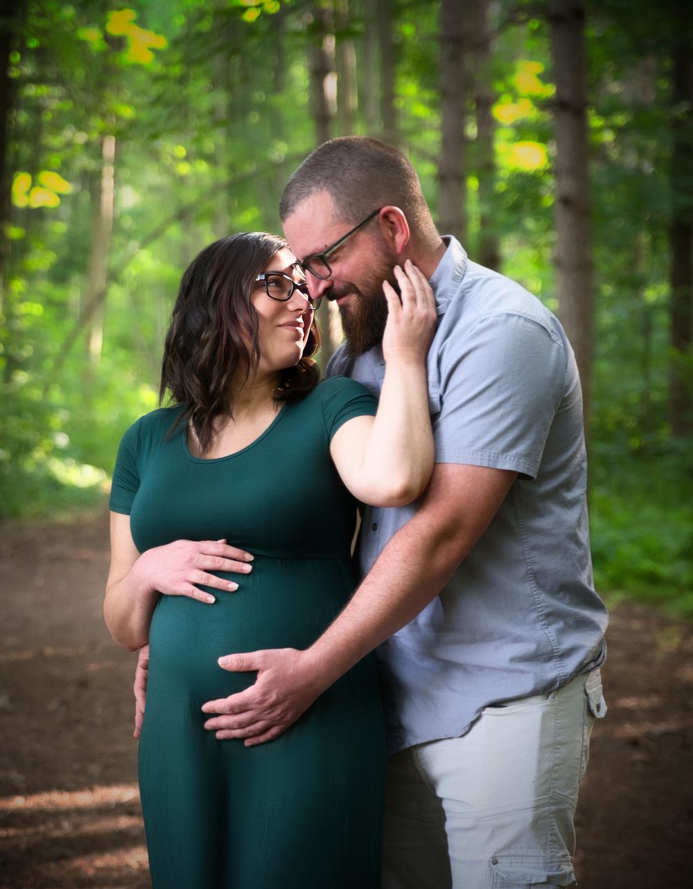 A tender maternity photo showing an intimate moment between a couple on a wooded path surrounded by lush greenery.