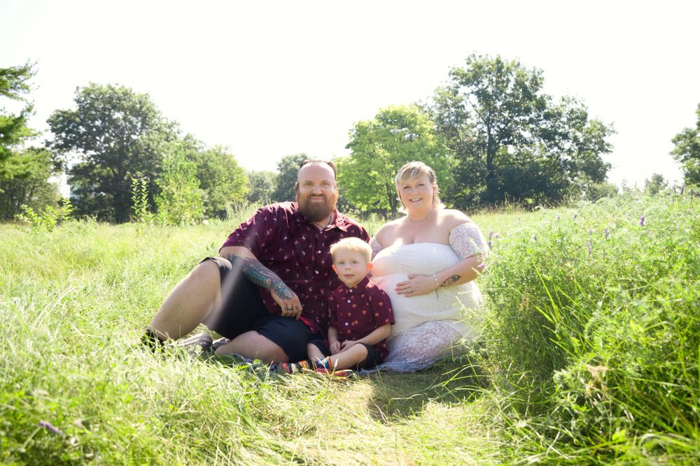 Family group resting together in a sunny summer meadow with tall grass and trees in the background.