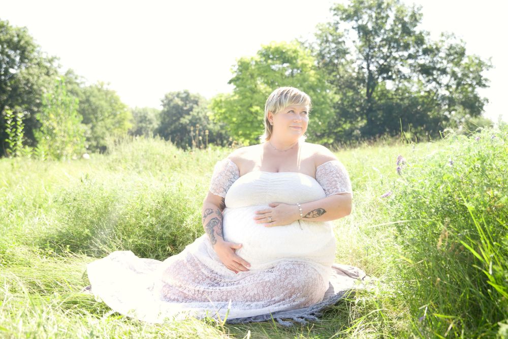 Dreamy maternity portrait in a sunny meadow with wildflowers and soft natural lighting.