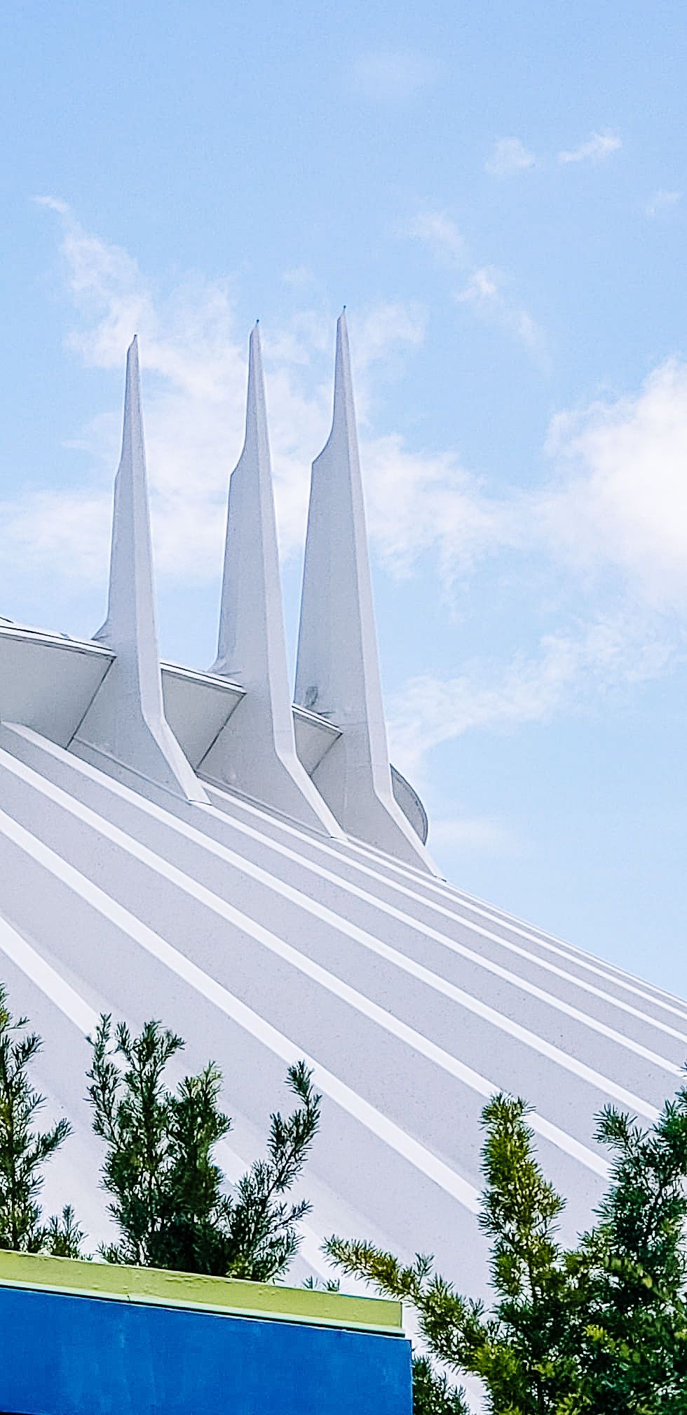 A series of four images showing white, modern architectural spires against a blue sky with trees in the foreground.