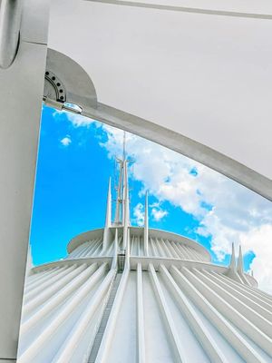 View looking up at Space Mountain's iconic white dome structure at Disney World against a bright blue sky with puffy clouds.