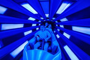 Passengers illuminated in bright blue light while riding through a futuristic looking tunnel attraction.